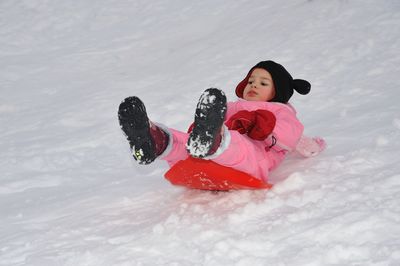 Full length of girl tobogganing on snow covered field