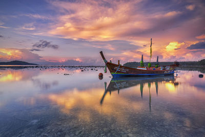 Fishing boats moored in sea against sky during sunset