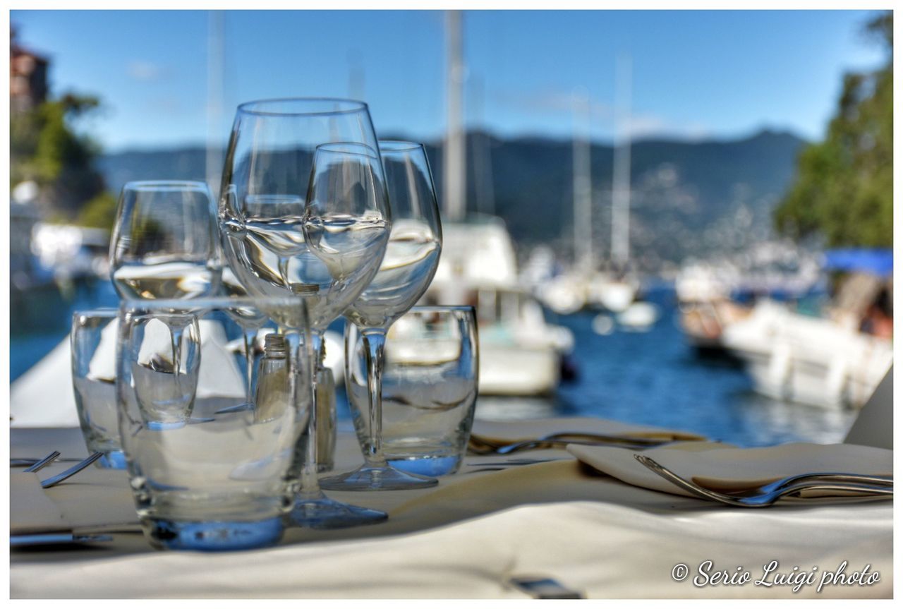 glass, table, water, drinking glass, setting, focus on foreground, household equipment, wineglass, transparent, glass - material, nature, place setting, no people, food and drink, day, transfer print, auto post production filter, restaurant, business, outdoors, luxury