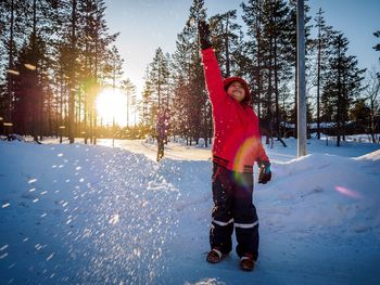 Boy throwing snow against trees during sunset