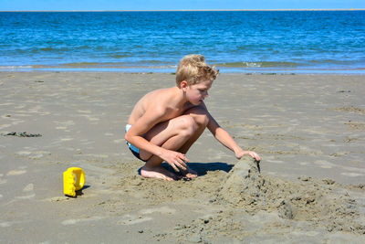 A little blond boy builds a sand castle in the sand on the beach in front of the sea