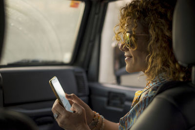 Smiling woman using mobile phone while sitting in car