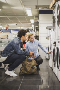 Mature owner explaining about washing machine to male customer in electronics store