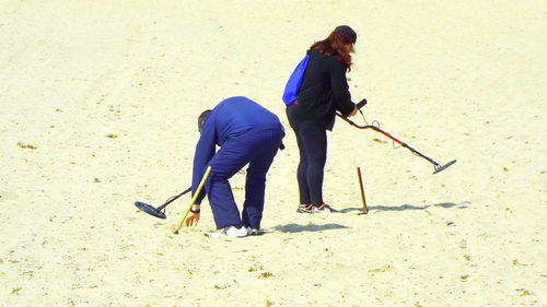 High angle view of man and woman searching with metal detector at beach