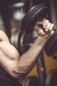 Cropped hand of man exercising with dumbbell at gym