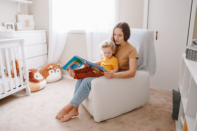 Mom reading book with baby boy toddler at home. early age children education development. 