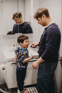 Father helping son brush his teeth