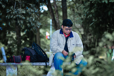 Side view of man using mobile phone while standing against trees