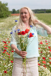 Beautiful middle-aged blonde woman stands among a flowering field of poppies