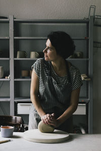 Female entrepreneur looking away while kneading clay in ceramics workshop