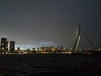 Illuminated city by river against sky at night