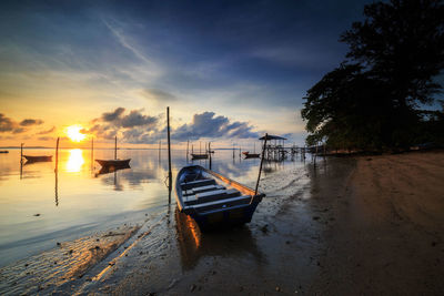 Boat moored on beach against sky during sunset