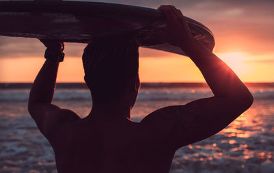 Close-up of man carrying surfboard on head while standing at beach