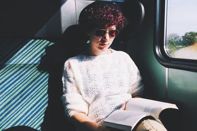 Young woman reading book while traveling train during sunny day