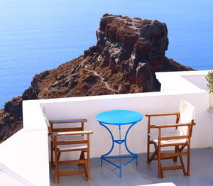 Table and chairs on rocks by sea against blue sky