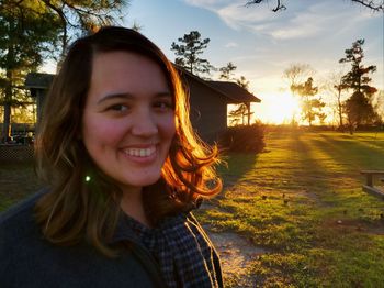 Portrait of smiling young woman on field against sky during sunset