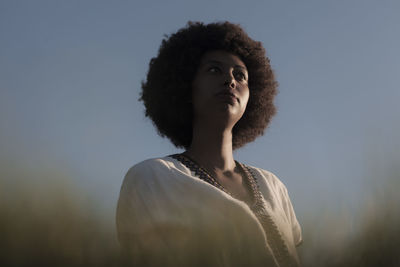 Portrait of young woman looking away against sky