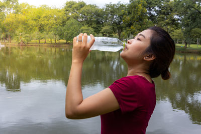 Side view of woman drinking water by lake