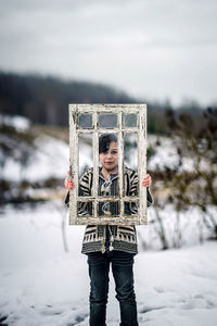 Low section of kid standing on snow holding window frame