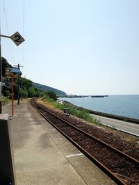 Railroad tracks by sea against clear sky