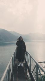 Full length portrait of woman standing on railing against sea