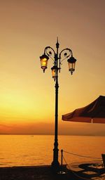 Street light by sea against sky during sunset