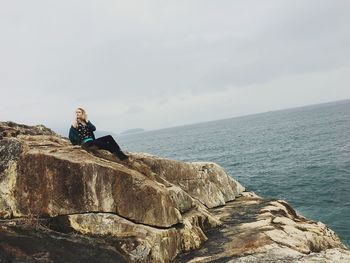 Man sitting on rock by sea against sky