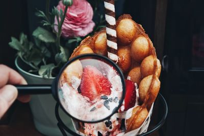 Close-up of hand holding magnifying glass by ice cream