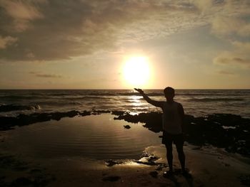Rear view of boy standing at beach during sunset