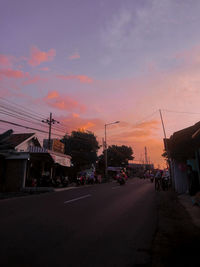 Cars on street against sky at sunset