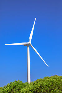 Low angle view of wind turbines on field against clear blue sky