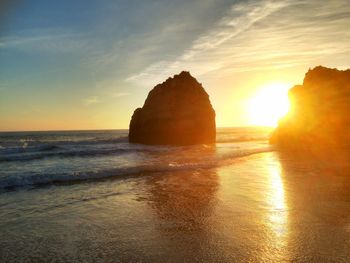 Rock formation on beach against sky during sunset