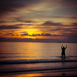 Silhouette man splashing water in sea against sky during sunset