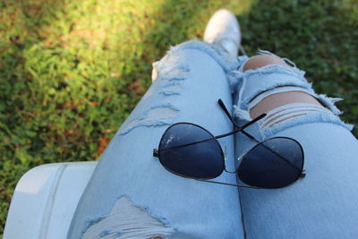 High angle view of sunglasses on lap of woman wearing torn jeans