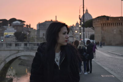 Woman standing in city against sky during sunset