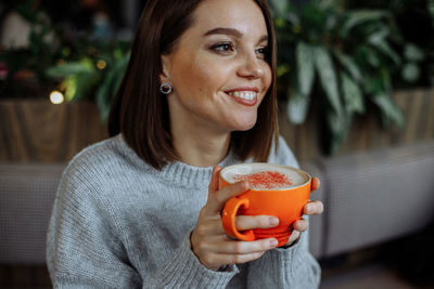 A young girl in a cafe drinks coffee from a bright orange mug