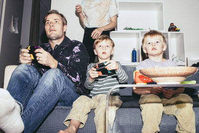 Father playing video game with son while sitting on sofa at home