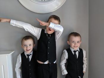 Portrait of smiling brothers wearing suits standing against wall at home