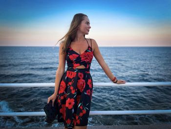 Woman standing by railing against sea against sky