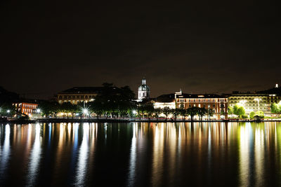 Illuminated buildings by mosque against sky at night