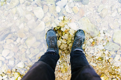 From above of unrecognizable crop traveler in trekking waterproof boots standing in lake with crystal clear water