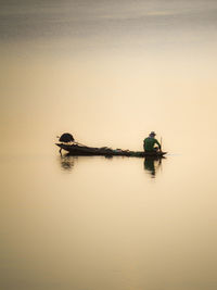 Man in boat on lake against sky during sunset