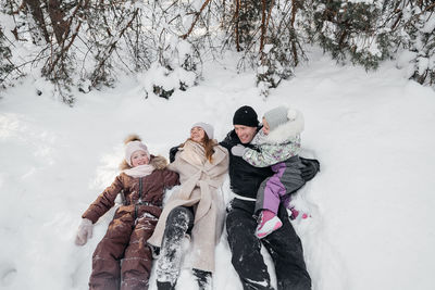 Dad and mom and daughters lying in the snow in the winter forest