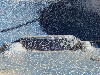 Blue mosaic bench on footpath against wall