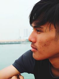 Close-up of young man looking away against sky