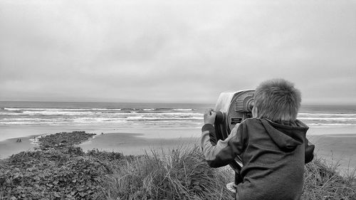 Rear view of boy looking through coin operated binoculars