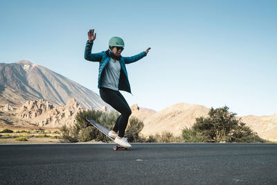 Woman performing stunt on skateboard against mountains