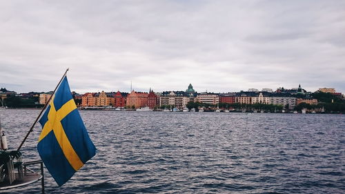 Swedish flag by lake against sky in city