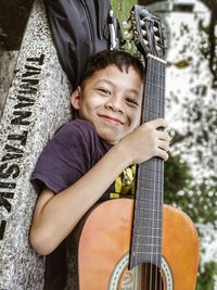 Portrait of smiling boy with guitar standing at concrete wall