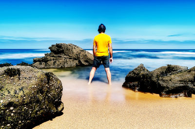 Rear view of man standing on rock by sea against sky